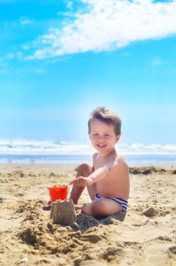Bir çocuk kumla oynar ve deniz kıyısında kumdan kaleler inşa eder. Yaz havası