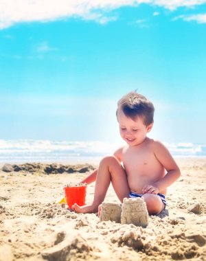 Bir çocuk kumla oynar ve deniz kıyısında kumdan kaleler inşa eder. Yaz havası