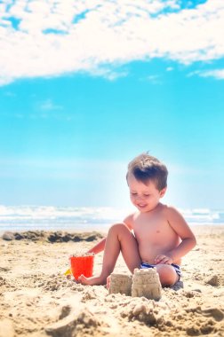 Bir çocuk kumla oynar ve deniz kıyısında kumdan kaleler inşa eder. Yaz havası