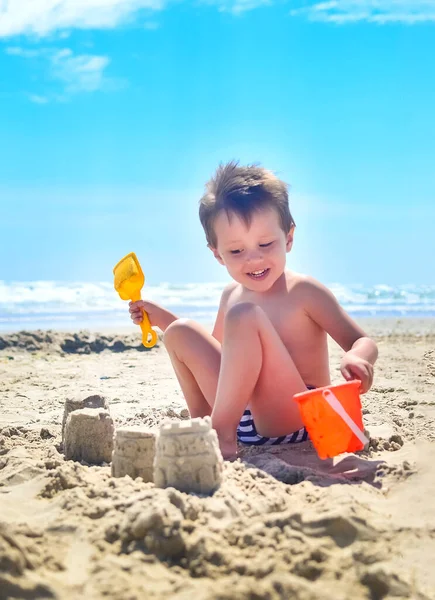 a boy plays with sand and builds sand castles on the seashore. summer mood