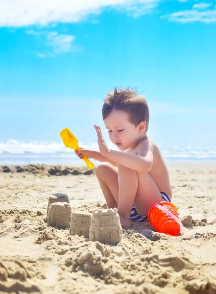 少年は砂で遊んで海岸に砂の城を築きます 夏の気分 — ストック写真