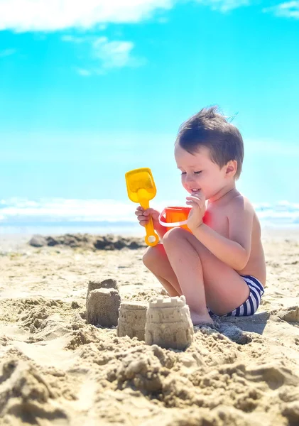 a boy plays with sand and builds sand castles on the seashore. summer mood