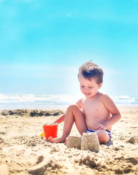 a boy plays with sand and builds sand castles on the seashore. summer mood