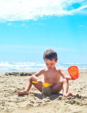 Bir çocuk kumla oynar ve deniz kıyısında kumdan kaleler inşa eder. Yaz havası