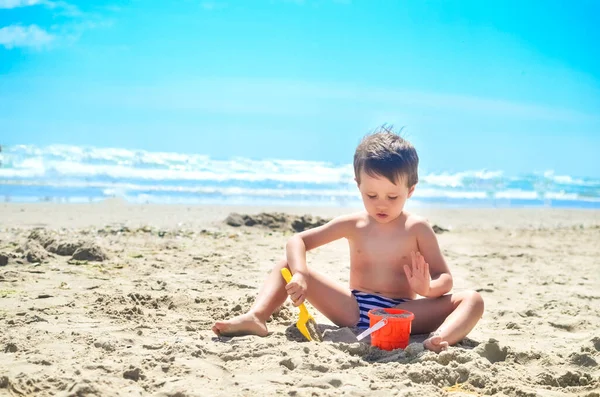 少年は砂で遊んで海岸に砂の城を築きます 夏の気分 — ストック写真