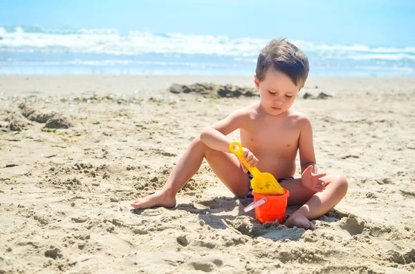 少年は砂で遊んで海岸に砂の城を築きます 夏の気分 — ストック写真
