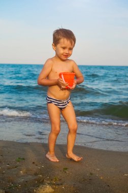 Mutlu bir çocuk sahilde suyun içinde oturuyor ve dalgalara su sıçratıyor. Bir çocuk denizin tadını çıkarır.
