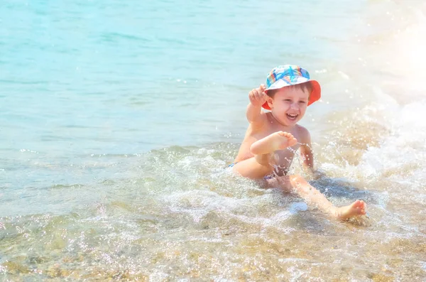 幸せな少年がビーチの水の中に座って波に飛び散る 子供は海を楽しむ — ストック写真