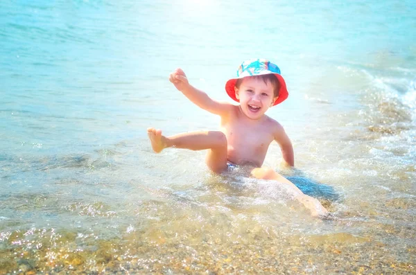幸せな少年がビーチの水の中に座って波に飛び散る 子供は海を楽しむ — ストック写真
