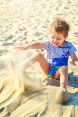 Neşeli çocuk deniz kenarında kumla oynuyor.