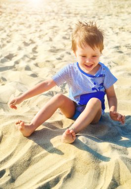 Neşeli çocuk deniz kenarında kumla oynuyor.