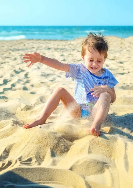 joyful boy plays with sand by the sea