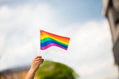 Gökyüzünde gökkuşağı bayrakları olan eşcinsel bir bilezik takan kadın eli. LGBT insanları, eşcinsel ilişkiler ve homoseksüel kavramlar 
