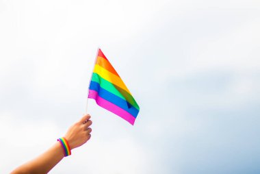  Gökyüzüne gökkuşağı bayraklı eşcinsel bir bilezik takan el. LGBT insanları, eşcinsel ilişkiler ve homoseksüel kavramlar 