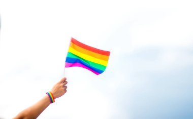  Gökyüzüne gökkuşağı bayraklı eşcinsel bir bilezik takan el. LGBT insanları, eşcinsel ilişkiler ve homoseksüel kavramlar 