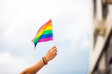  Gökyüzüne gökkuşağı bayraklı eşcinsel bir bilezik takan el. LGBT insanları, eşcinsel ilişkiler ve homoseksüel kavramlar 