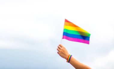  Gökyüzüne gökkuşağı bayraklı eşcinsel bir bilezik takan el. LGBT insanları, eşcinsel ilişkiler ve homoseksüel kavramlar 