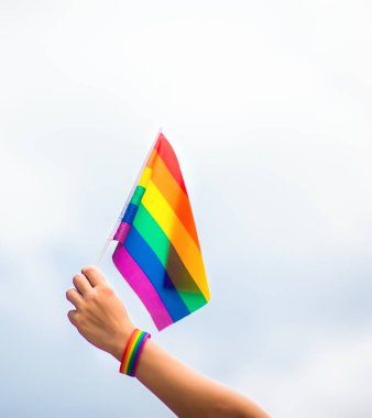  Gökyüzüne gökkuşağı bayraklı eşcinsel bir bilezik takan el. LGBT insanları, eşcinsel ilişkiler ve homoseksüel kavramlar 