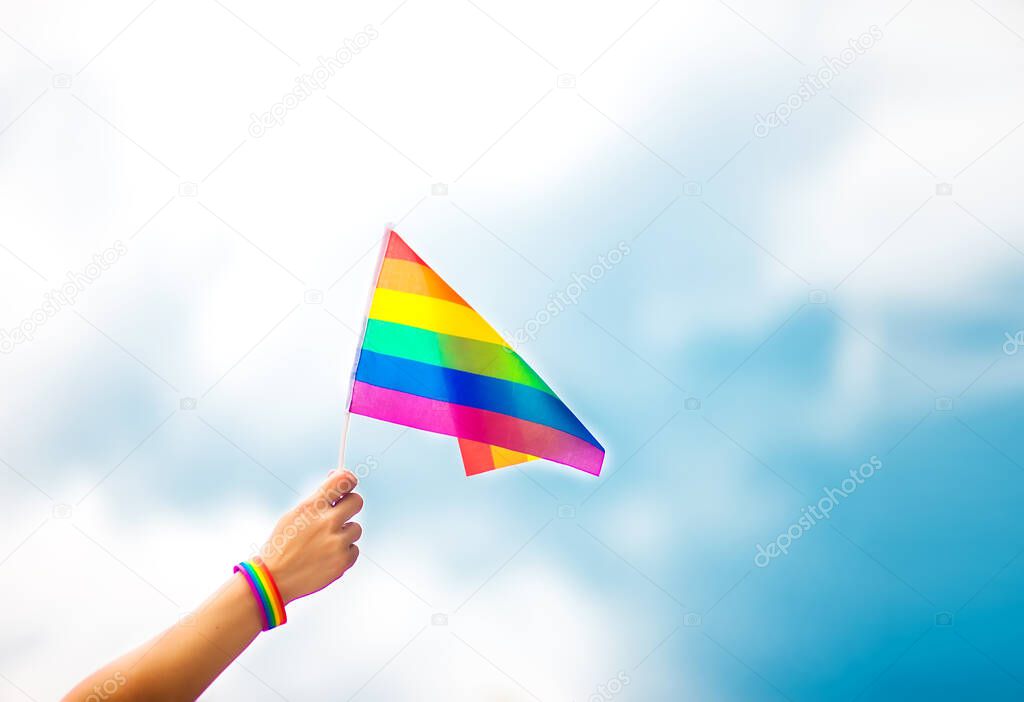  hand wearing a gay pride bracelet with rainbow flags against the sky. LGBT people, same-sex relationships and homosexual concepts 