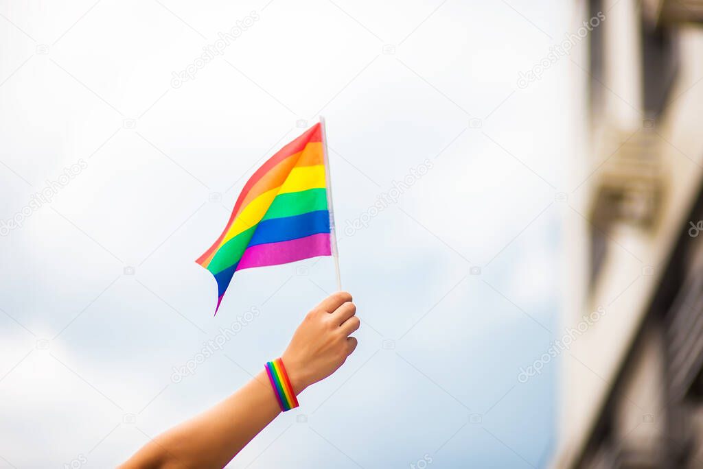  hand wearing a gay pride bracelet with rainbow flags against the sky. LGBT people, same-sex relationships and homosexual concepts 