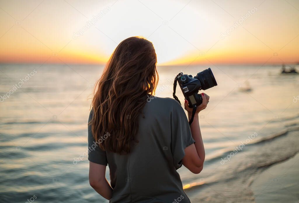 girl photographer with a camera in hand against the background of the sea and sunset