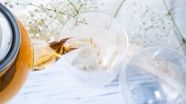 Cam çaydanlıktan çift duvar bardaklarına siyah çay dökülüyor. Altın çay. Boş kupalar. Parlak beyaz ahşap masa. Üst görünüm