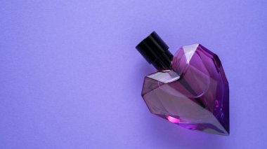 Mor arka planda cam şişede moda parfümü. Kalp şişesi şeklinde. Kırmızı şişe. Tutkulu bir parfüm. İzole edilmiş