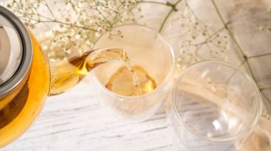 Şeffaf cam çaydanlıktan cam fincana altın çay dökülüyor. Bardağa siyah çay dolduran cam çaydanlık. Beyaz ahşap masa