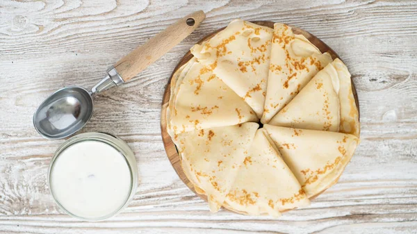 Frische französische Crêpes serviert mit saurer Sahne im Glas und Löffel zum Frühstück auf weißem Holztisch — Stockfoto