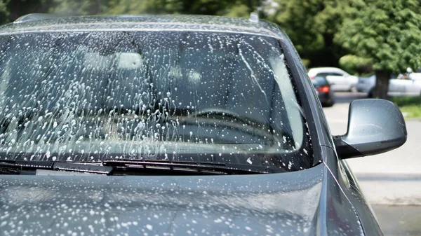 Full biltvätt vid självbetjäningen. Stänkta droppar vatten från en spruta som tvättar bilen. Vindrutan. Vitt skum — Stockfoto