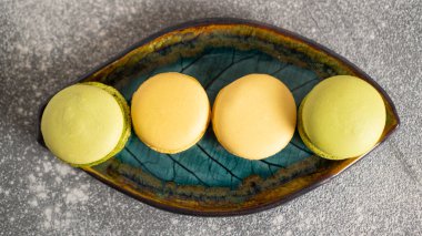 Makarnalar, gri beton bir masada yaprak şeklinde bir tabakta sıra sıra dizilir. Keyifli bir ruh hali için lezzetli kekler