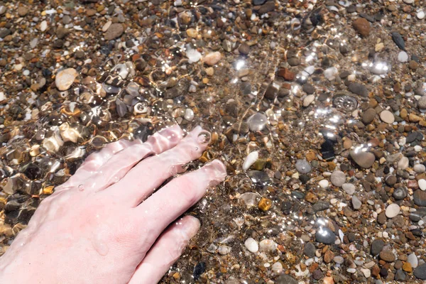 Çakıl taşları ve el suyun altında. Deniz yüzeyi. Suyun altındaki el, temiz şeffaf suyun altındaki çakıl taşlarına dokunuyor. — Stok fotoğraf