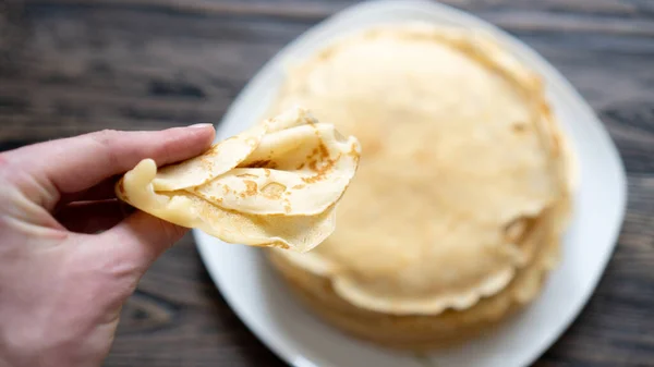 Hand hält frisch gebackene goldene Crêpes. Pfannkuchen zu einem Dreieck gefaltet. Leckeres traditionelles Frühstück — Stockfoto