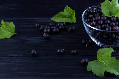 Siyah frenk üzümü ve koyu ahşap arka planda yeşil yapraklar. Frenk üzümü ve yeşil yapraklı arka plan. Frenk üzümü makrosu.