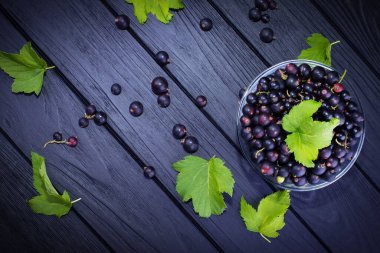 Siyah frenk üzümü ve koyu ahşap arka planda yeşil yapraklar. Frenk üzümü ve yeşil yapraklı arka plan. Frenk üzümü makrosu.