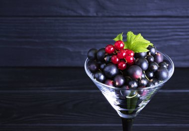 Siyah frenk üzümü ve koyu ahşap arka planda yeşil yapraklar. Frenk üzümü ve yeşil yapraklı arka plan. Frenk üzümü. Yakın plan.