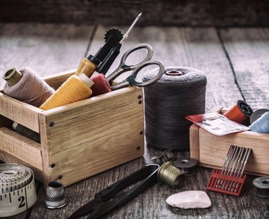Aksesuar dikme konsepti. Eski ahşap bir yüzeye dikiş aletleri, makaralar, düğmeler, iğneler, iğneler, iğne ve terziler için aksesuarlar dikmek. Retro biçimi