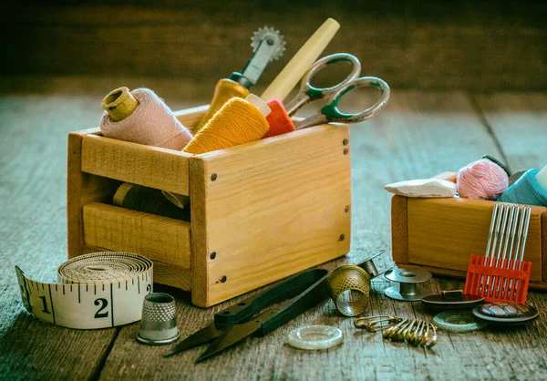 The concept of sewing accessories. Sewing tools and accessories for sewing threads, spools, scissors, buttons, needles, pin and tailor meter on an old wooden surface. Retro style.