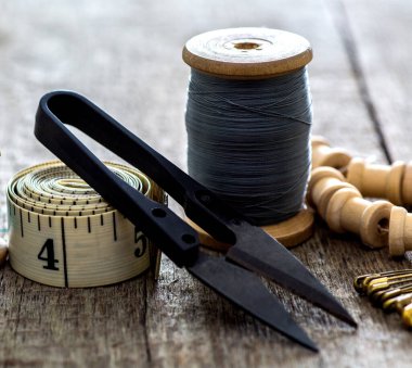 Eski ahşap bir yüzeye dikiş dikmek için terzi kurdele aletlerinin, yüksük ve makasın yaratıcı görüntüsü. Kavram. Seçici odak.
