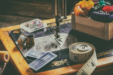 Eski bir dikiş makinesi, dikiş, makas, iğne ve masanın üstüne bir terzi bandı koymak için aksesuarlar. Aksesuar dikme konsepti. Retro tonlama