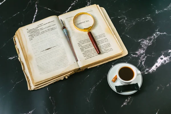 antique travel book with magnifying glass on marble top and coffee cup