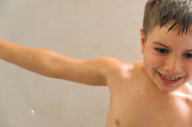 Çocuk banyoda duşla oynuyor.