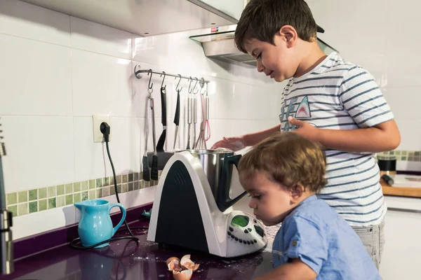 Two children preparing pancakes with a kitchen robot.