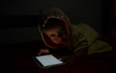 dítě ležící v posteli v županu sledující videozáznamy tabletu..