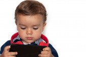 gyermek néz videókat a mobiltelefon piros fejhallgató és sötétkék ing