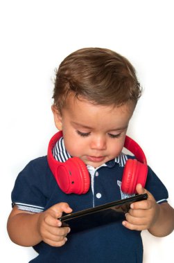 Çocuk cep telefonundan kırmızı kulaklıklı ve koyu mavi gömlekli videolar izliyor