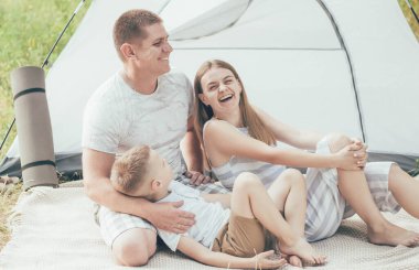 Aile nehir kıyısında dinleniyor. Çadırda baba ve oğul gülümsüyor.