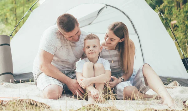 Family resting with tent outdoors dad hugs mom at boy smiling