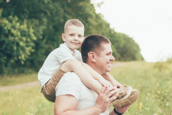 Dad and son are walking in nature, dad is holding son on his shoulders and son is smiling