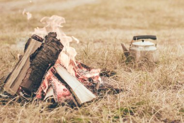 Arka planda bir şenlik ateşi yanıyor. Bir çaydanlık var.
